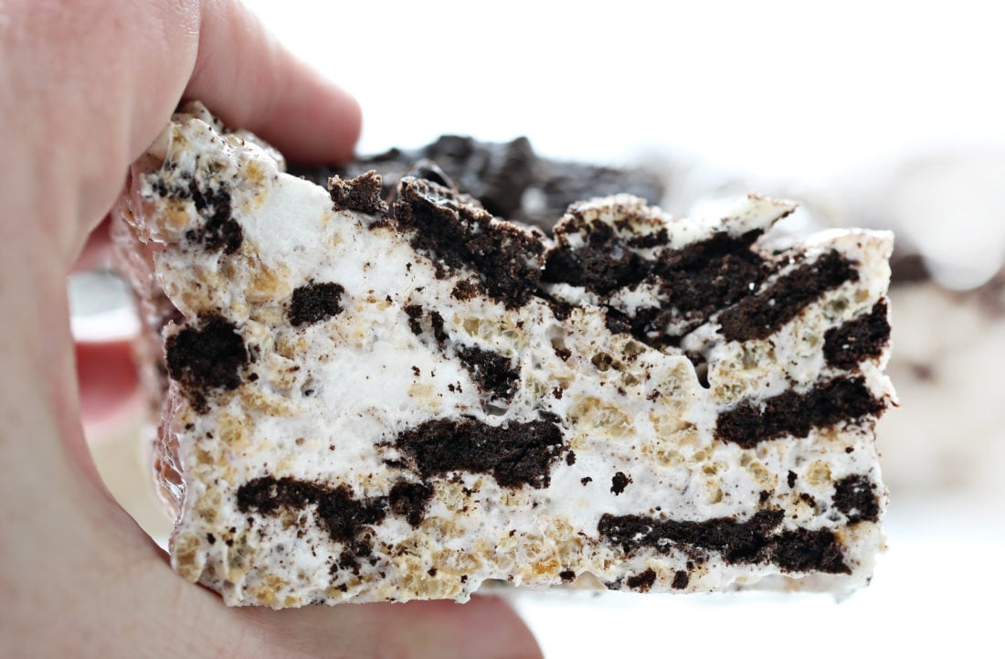The best no-bake desserts to get your sweet tooth through the summer! no bake, no bake desserts, desserts, recipes, cheesecake, cookies, bars, cake, pudding, mousse, puppy chow, muddie buddies, rice krispy bars, dessert, memorial day dessert, labor day desserts, i am baker, iambaker Oreo Rice Krispy Bar Held In Hand Very Close Up.