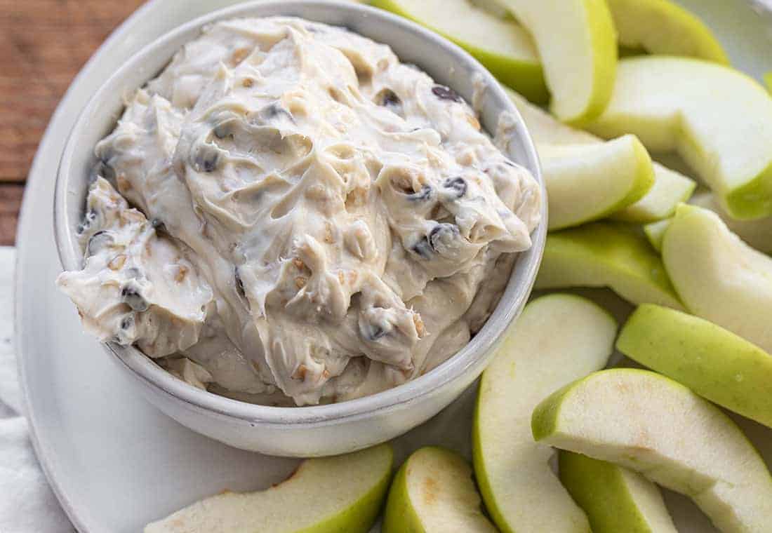 Apple Toffee Dip is a cream cheese-based, no-bake dip that is loaded with toffee bits and chocolate chips that is as easy to put together as it is delicious! Easy Dip, Apple Dip, Green Apple Dip, Col Dips, Appetizer, i am baker, iambaker, recipes Bowl of Apple Toffee Dip on Plate with Apple Slices