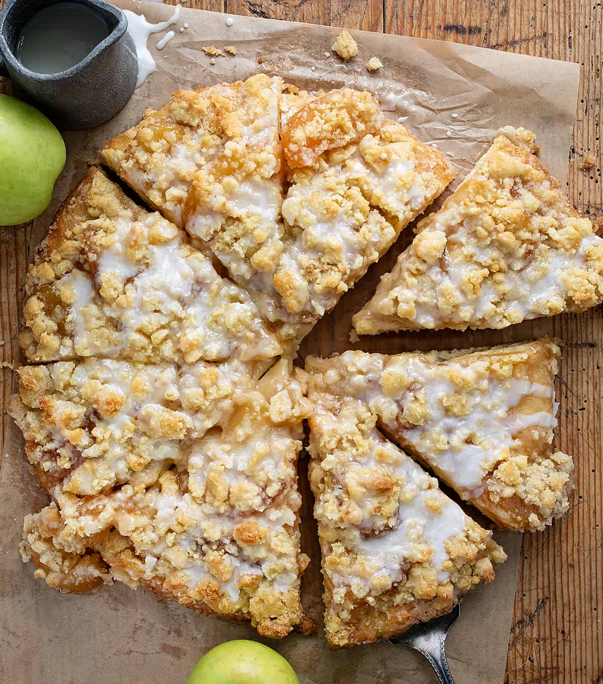 Apple Dessert Pizza is a delightful and unique treat that combines the flavors of a classic apple pie with the fun and convenience of a pizza. It starts with a soft focaccia bread crust topped with cinnamon butter spread, apple pie filling, and crumble topping for a little crunch. And then, a simple glaze is drizzled over the top. It will satisfy your sweet tooth with its cinnamon apple flavor and sweet glaze! Overhead of Apple Dessert Pizza Cut Into Pieces.