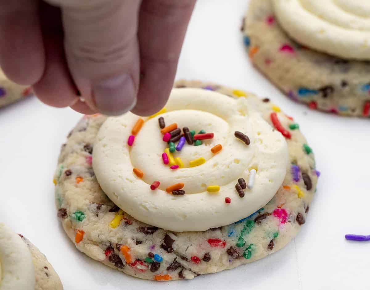 Birthday Cookies are chilled, but soft cookies that are loaded with colorful sprinkles, both chocolate and white chocolate chips, and topped with buttercream frosting. Cookies, Baking, Dessert, Birthday Cookies, Cookies with Frosting, Crumbl copycat cookie, birthday cookie recipes, cookie recipes, i am baker, iambaker Adding Sprinkles to Birthday Cake Cookies