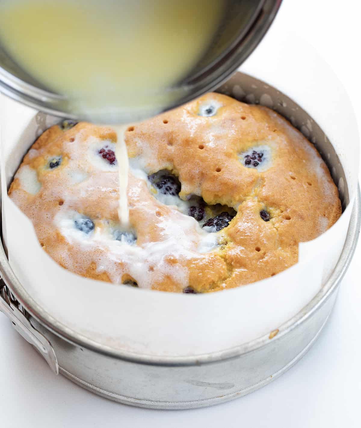 Blackberry Breakfast Cake is a cake filled with fresh blackberries, baked and then drenched in a warm sweet milk mixture for an incredibly moist and flavorful bite! It's a delicious morning treat alongside a cup of coffee, but regardless of the name, it's not just for breakfast! It can also be enjoyed as an afternoon snack or as a dessert after any meal! Pouring Milk Butter Mixture Over Blackberry Breakfast Cake.