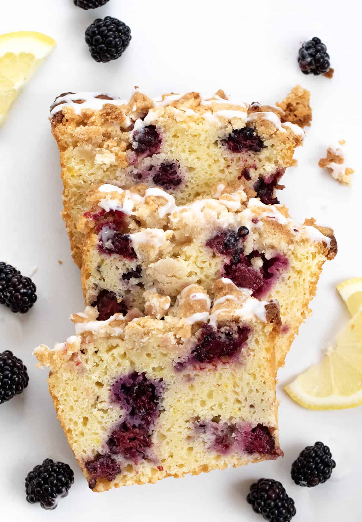 Blackberry Lemon Loaf is a moist, cake-like loaf with lots of fresh blackberries and tangy lemon flavor, topped with a buttery, crumbly topping. And then, a sweet glaze is drizzled over the loaf. Enjoy a slice anytime you crave a sweet and zesty treat Pieces of Blackberry Lemon Loaf on a White Counter.