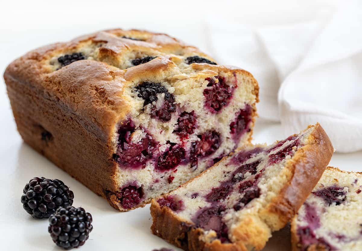 Blackberry Loaf is a soft and tender quick bread loaded with fresh blackberries and drizzled with an optional sweet glaze. Whether you're planning a casual brunch, afternoon tea, or simply a gathering with friends, this blackberry loaf fits the occasion perfectly! Plus, it is easy to make! I like to pair a slice with a cup of coffee for a delightful snack. Close up of Blackberry Loaf with Some Pieces Cut and Showing Inside Texture.