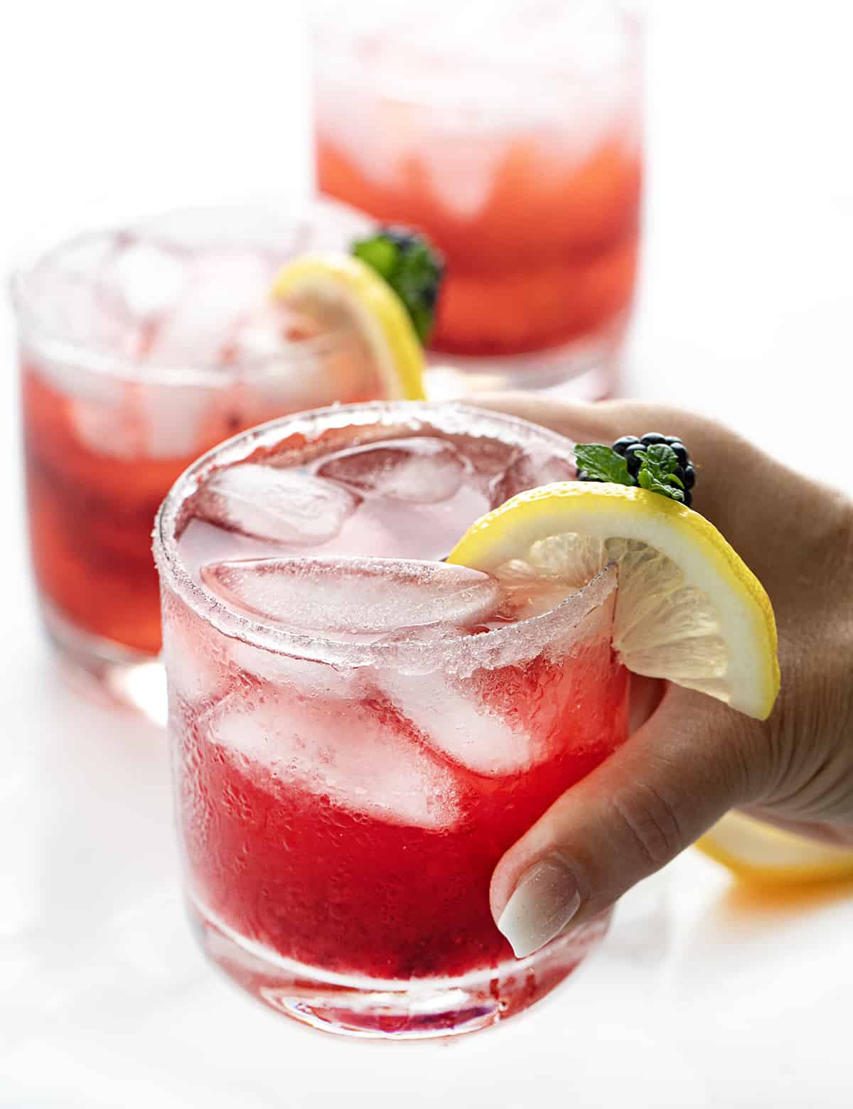 Blackberry Moscato Cocktail is a bubbly and refreshing alcoholic beverage made with fresh blackberries, lemon juice, sugar, lemon-lime soda, and Moscato d'Asti wine. This delightful drink is also known as Berry Breeze, Moscato Berry Smash, Lemonberry Fizz, and Blackberry Moscato Lemonade. No matter what you call it, you get a sweet, tangy, and fizzy concoction bursting with fruity flavors in every sip! Hand Picking up a Blackberry Moscato Cocktail.