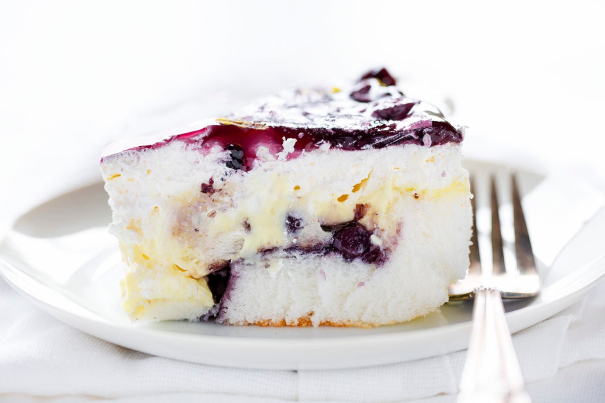 The best no-bake desserts to get your sweet tooth through the summer! no bake, no bake desserts, desserts, recipes, cheesecake, cookies, bars, cake, pudding, mousse, puppy chow, muddie buddies, rice krispy bars, dessert, memorial day dessert, labor day desserts, i am baker, iambaker Blueberry Lemon Heaven Dessert On a Plate Showing Layers of Angel Food Cake, Blueberry Pie Filling, and Lemon Pudding.