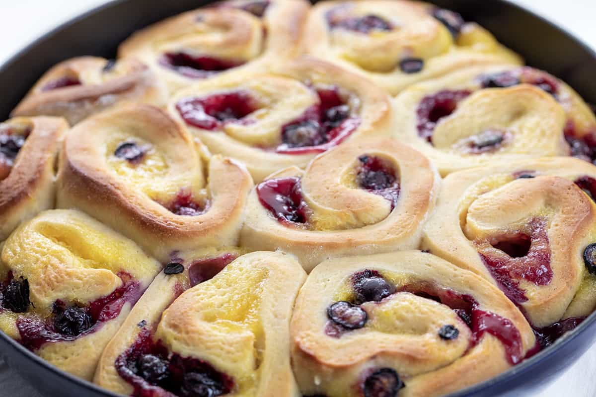 Blueberry Lemon Skillet Rolls are super soft rolls baked with lemon curd and fresh blueberries, then topped with a homemade blueberry sauce. They are the perfect treat for breakfast, brunch, or anytime you are craving one! I used an overnight dough to make things really easy for busy people, but no fear, there are also instructions for quicker use CLose up of Blueberry Lemon Skillet Rolls in a Pan Just out of the Oven.