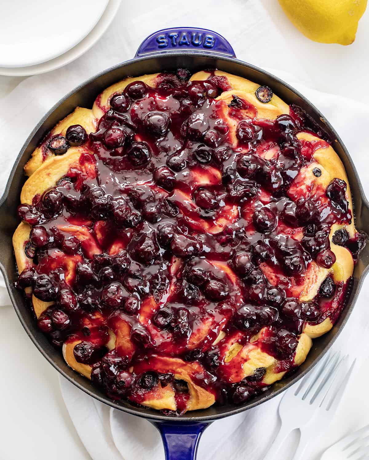 Blueberry Lemon Skillet Rolls are super soft rolls baked with lemon curd and fresh blueberries, then topped with a homemade blueberry sauce. They are the perfect treat for breakfast, brunch, or anytime you are craving one! I used an overnight dough to make things really easy for busy people, but no fear, there are also instructions for quicker use Blueberry Lemon Skillet Rolls in Skillet on a White Counter.