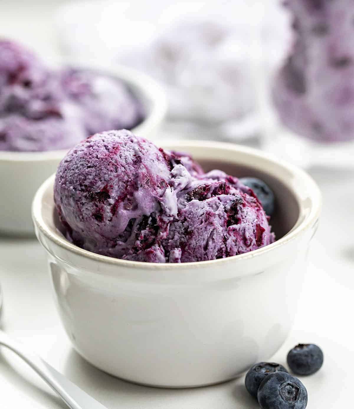 Blueberry No-Churn Ice Cream is super flavorful homemade ice cream made with fresh blueberries. The best part? No ice cream machine is required! Homemade Ice Cream, No Churn Ice Cream, Blueberry No Churn Ice Cream, Fresh Blueberry Ice Cream, Fruity Ice Cream, Dessert, No Bake Dessert, Blueberry Desserts, Easy Dessert, recipes, i am baker, iambaker White Bowl Filled with Blueberry No-Churn Ice Cream with White Spoon and Blueberries on Counter.