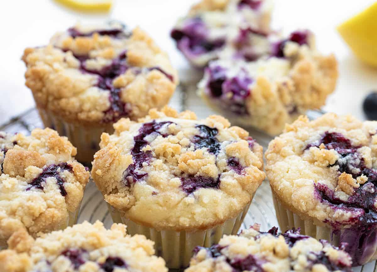 Blueberry Lemon Crumb Muffins are moist and tender muffins loaded with fresh blueberries and lemon flavor, topped and baked with a crispy, buttery crumble. They are the perfect sweet snack, dessert, or breakfast! Blueberry Lemon Muffins on a White Counter with Fresh Lemon Slice and Blueberries.