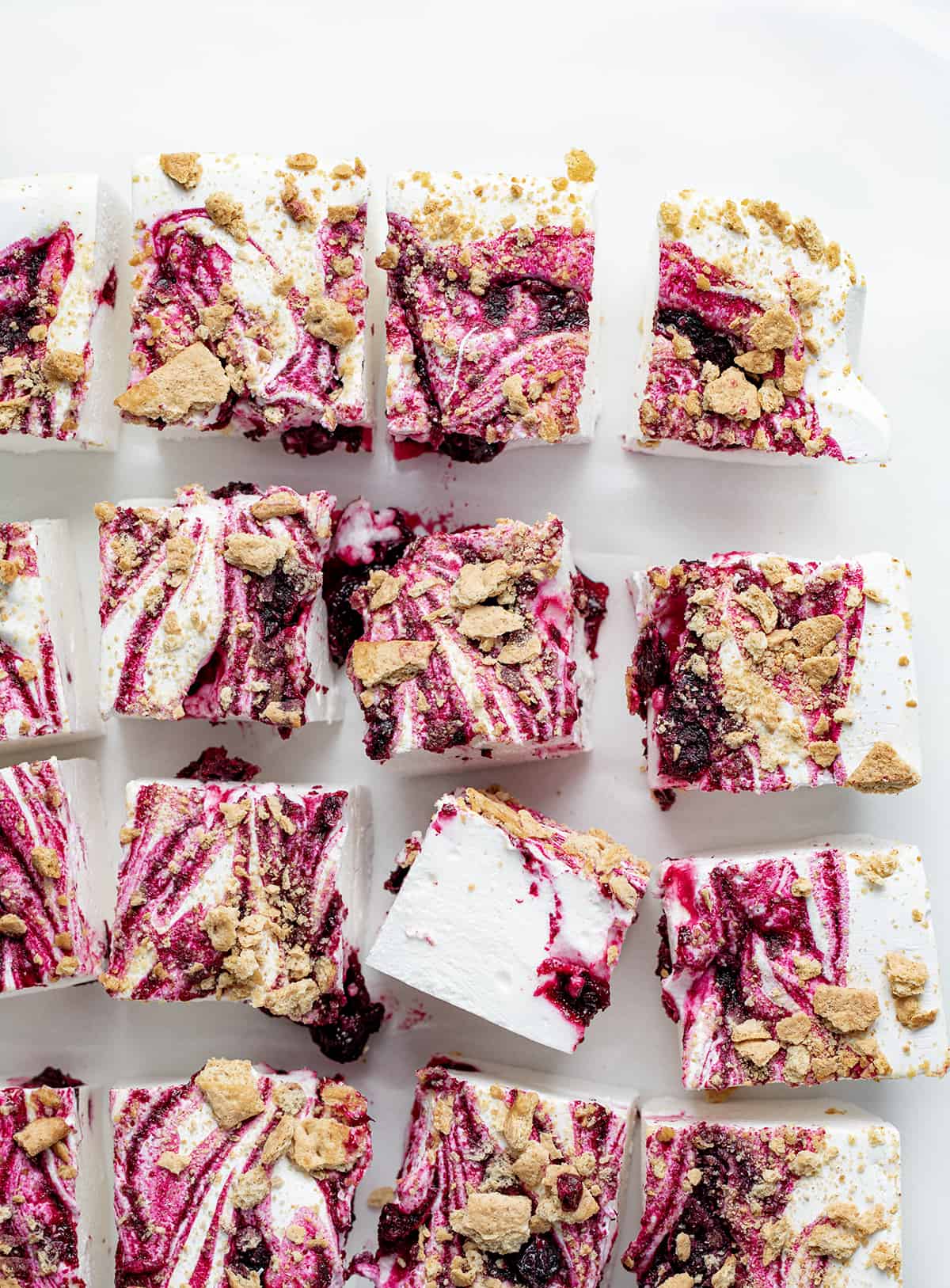 Blueberry Marshmallows are super fluffy homemade marshmallows marbled with blueberry syrup and topped with crushed graham crackers. I was going for a "Blueberry Cheesecake Marshmallow" and I think the addition of the graham crackers really works! The unique combination of flavors and textures elevates them (literally) to the level of gourmet marshmallows, making them a must-try for anyone who loves a sweet treat. Pieces of Gourmet Blueberry Marshmallows On a White Surface and Cut into Squares.
