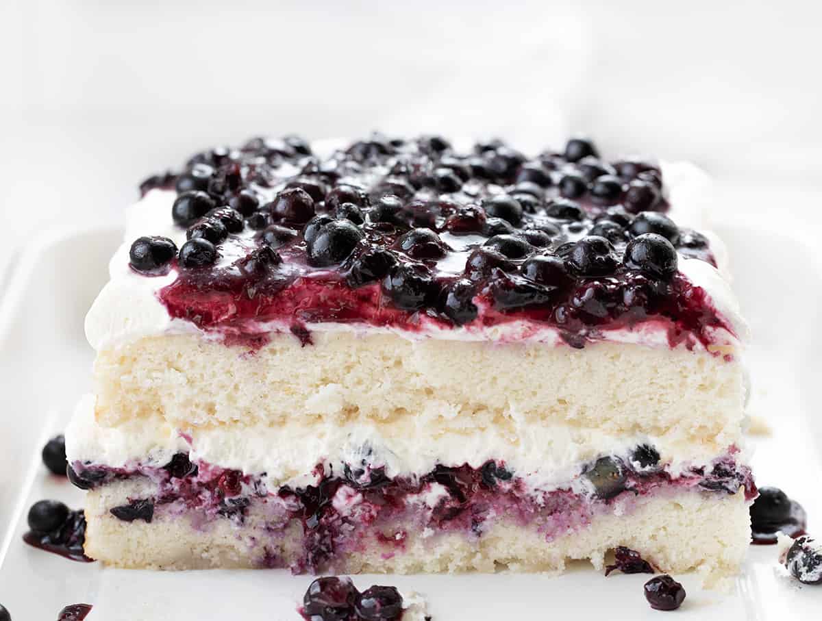 Sheet Pan Blueberry Shortcake Cake starts with a delicious white cake that is cut in half and layered with a homemade blueberry mixture and whipped cream cheese topping. It's a delightful dessert, combining the tender cake base with a sweet and tangy blueberry topping. The creamy whipped topping adds a luxurious and creamy element to the dessert, making it a perfect treat for any occasion. Cut Into Sheet Pan Blueberry Shortcake Cake Showing Tender Layers.