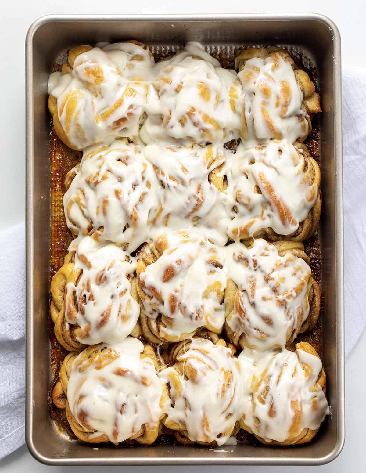 Braided Cinnamon Rolls are a delightful variation of the classic sweet rolls with a beautifully woven braided appearance, drizzled with a cream cheese glaze. They are so soft and the combination of cinnamon, brown sugar, and butter in each layer makes them so irresistible! They are wonderful without the glaze, too. You can also make these in an air fryer! Frosted Braided Cinnamon Rolls in a Pan on a White Counter from Overhead.