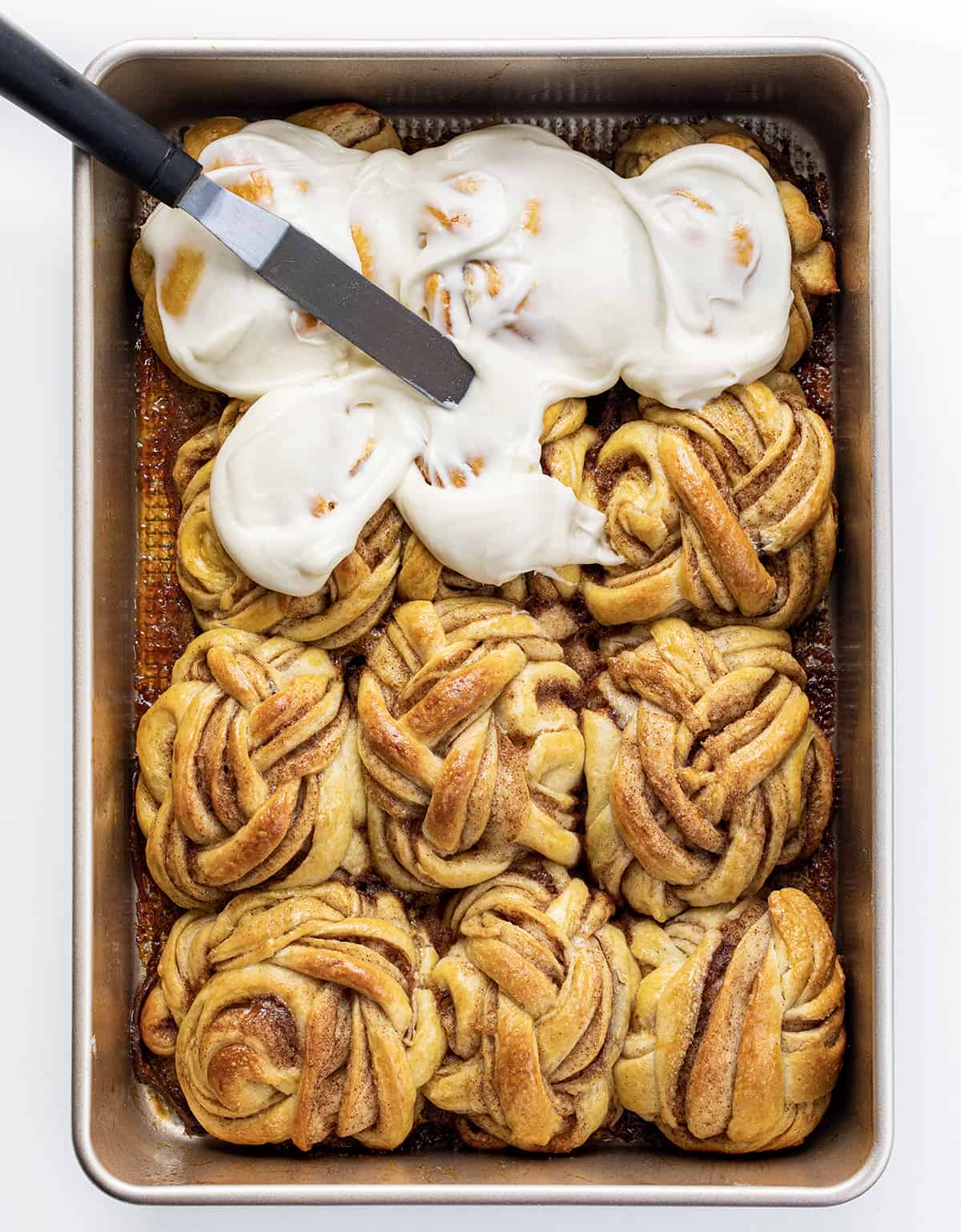Braided Cinnamon Rolls are a delightful variation of the classic sweet rolls with a beautifully woven braided appearance, drizzled with a cream cheese glaze. They are so soft and the combination of cinnamon, brown sugar, and butter in each layer makes them so irresistible! They are wonderful without the glaze, too. You can also make these in an air fryer! Braided Cinnamon Rolls in Pan After Baking Showing Them Partially Frosted.