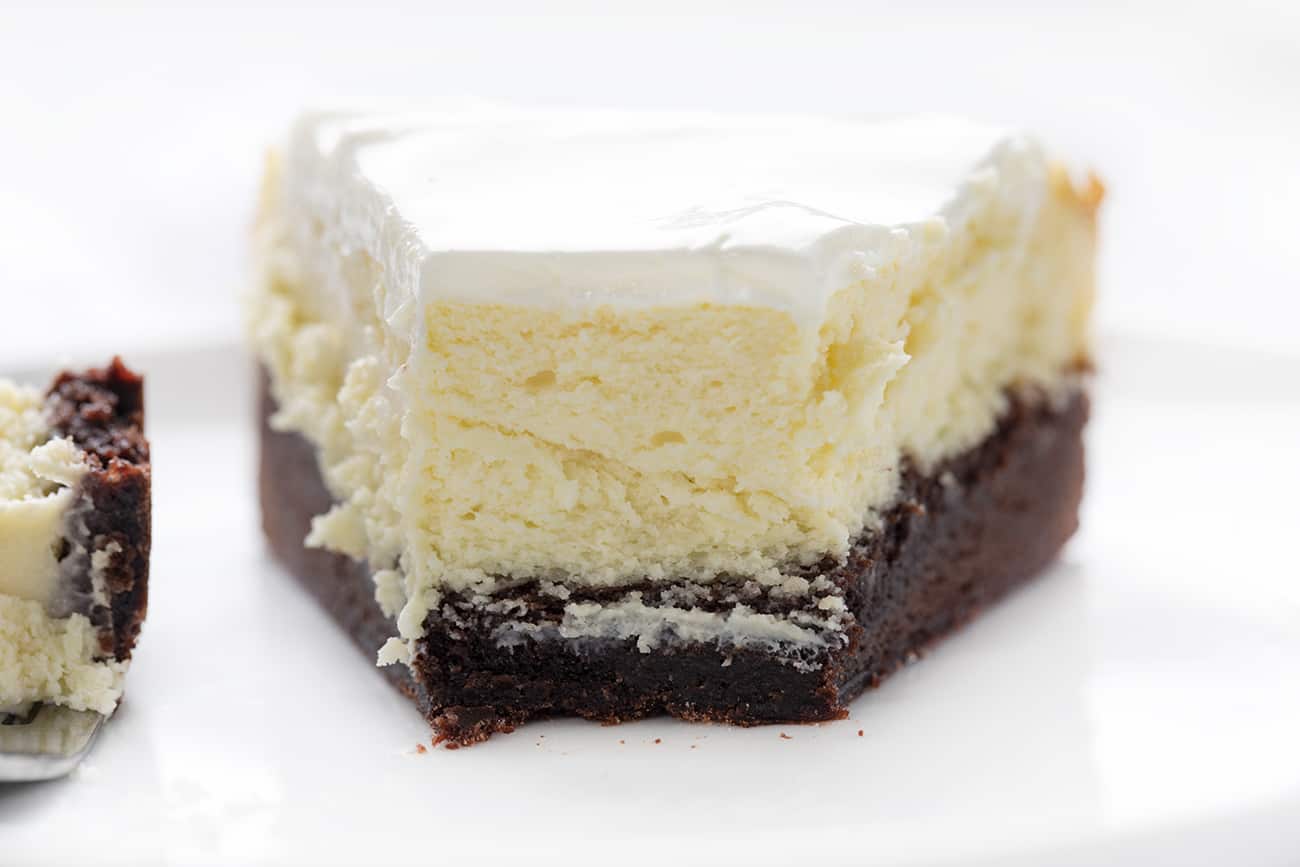 Brownie Bottom Cheesecake is a rich and creamy cheesecake that is layered on top of a sweet chocolate brownie mixture bottom, covered with a sweet sour cream topping! Cheesecake, Brownie Bottom Cheesecake, Brownie Cheesecake, Dessert, Baking, How to Make Brownie Bottom Cheesecake, How to Make Sour Cream Glaze, i am baker, iambaker View of Cut Into Brownie Bottom Cheesecake showing the Inside and Fork next to it