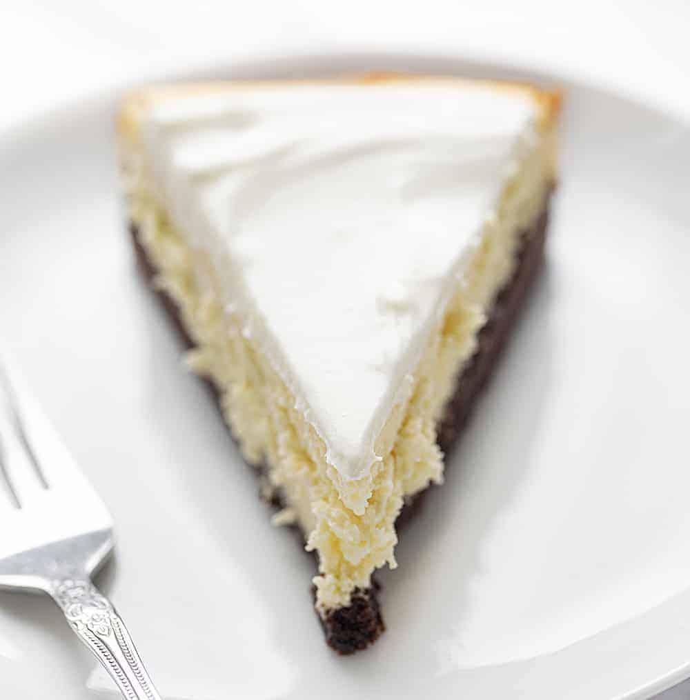 Brownie Bottom Cheesecake is a rich and creamy cheesecake that is layered on top of a sweet chocolate brownie mixture bottom, covered with a sweet sour cream topping! Cheesecake, Brownie Bottom Cheesecake, Brownie Cheesecake, Dessert, Baking, How to Make Brownie Bottom Cheesecake, How to Make Sour Cream Glaze, i am baker, iambaker One PIece of Brownie Bottom Cheesecake on White Plate with Fork Next to It