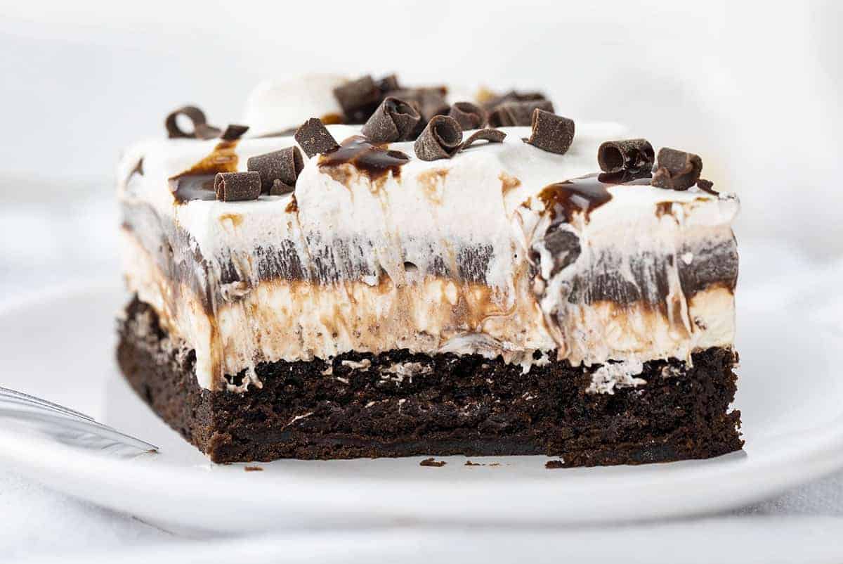 Brownie Pudding Dessert is a decadent layered dessert that starts with the perfect brownie, topped with a cream cheese and chocolate pudding layer, finished off with cool whip and more chocolate! Brownie, Chocolate Pudding, Brownie Pudding Dessert, Brownie Dessert, Dessert, Pudding Dessert, Summer Desserts, Fall Desserts, Winter Dessert, Dessert Recipes, Brownie Recipes, Layered Dessert, i am baker, iambaker Piece of Brownie Pudding Dessert with Bite Removed and Fork Resting on Plate