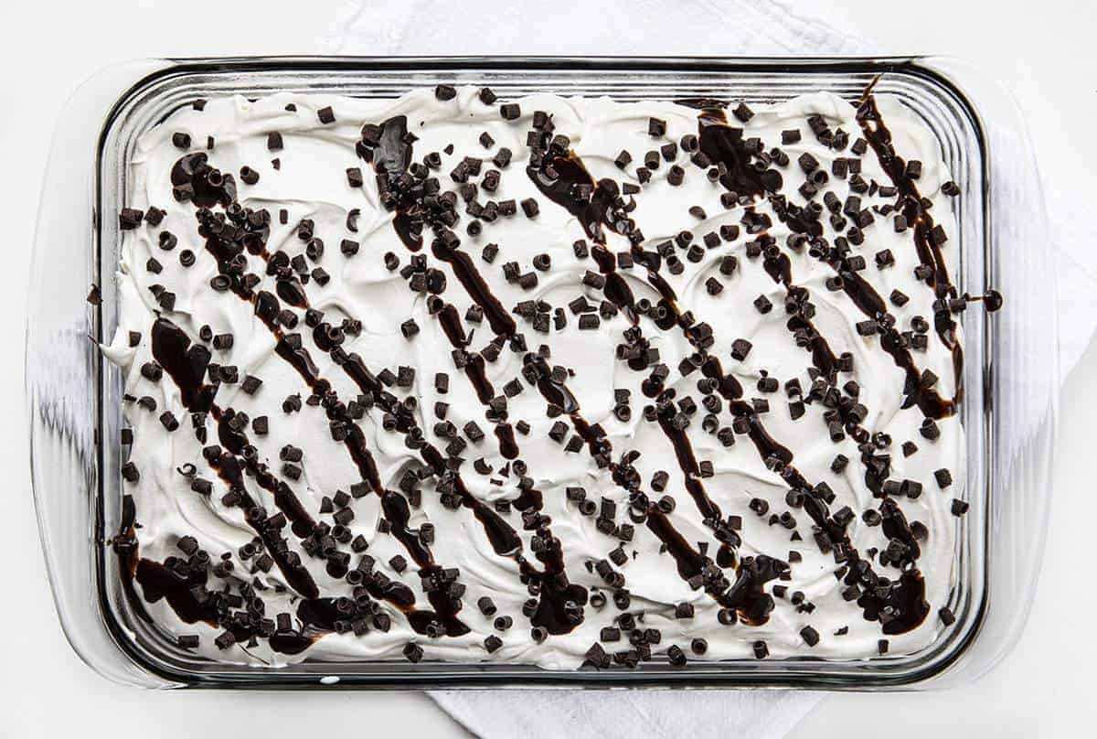 Brownie Pudding Dessert is a decadent layered dessert that starts with the perfect brownie, topped with a cream cheese and chocolate pudding layer, finished off with cool whip and more chocolate! Brownie, Chocolate Pudding, Brownie Pudding Dessert, Brownie Dessert, Dessert, Pudding Dessert, Summer Desserts, Fall Desserts, Winter Dessert, Dessert Recipes, Brownie Recipes, Layered Dessert, i am baker, iambaker Overhead Image of Brownie Pudding Dessert Showing Chocolate Curls and Chocolate Syrup on Top of Whipped Cream