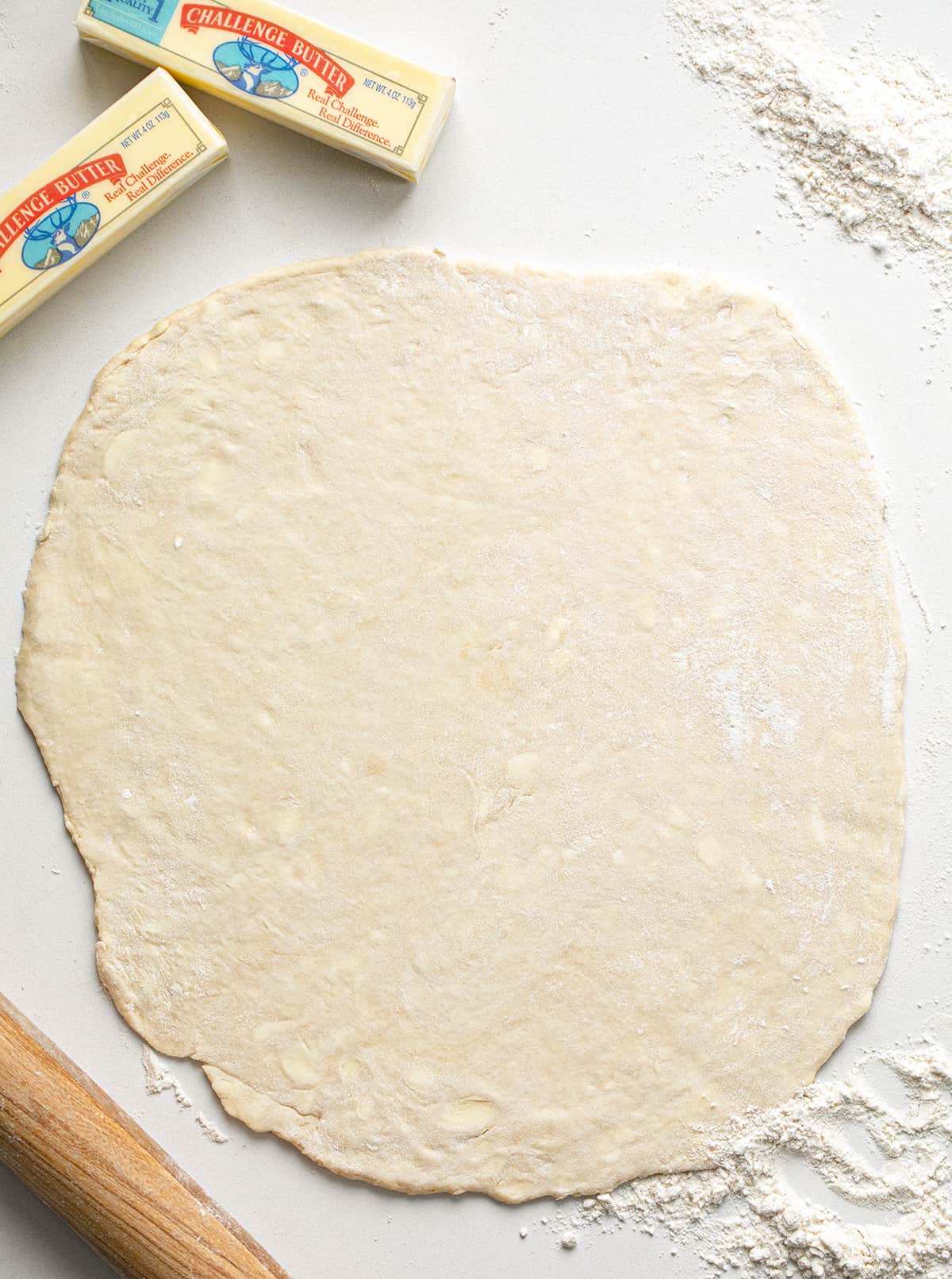 Do you want the best no-fail ALL BUTTER Pie crust? Professional bakers agree, this one tastes the best! All Butter Pie Dough Rolled Out on a Counter with Butter, a Rolling Pin, and Flour Next to It.
