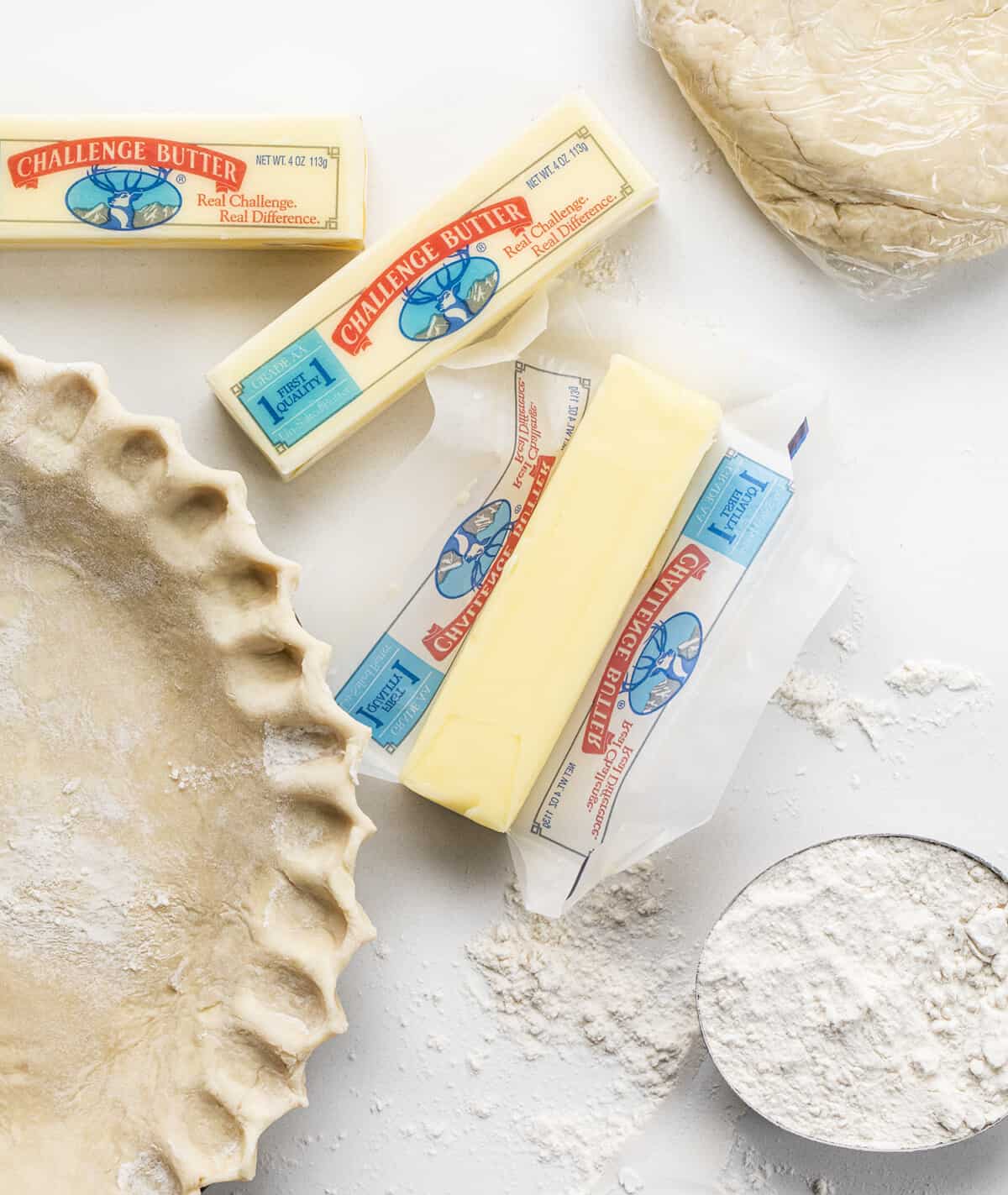 Do you want the best no-fail ALL BUTTER Pie crust? Professional bakers agree, this one tastes the best! Butter Pie Crust in a Pan with Butter, Flour, and Extra Crust Next to It.