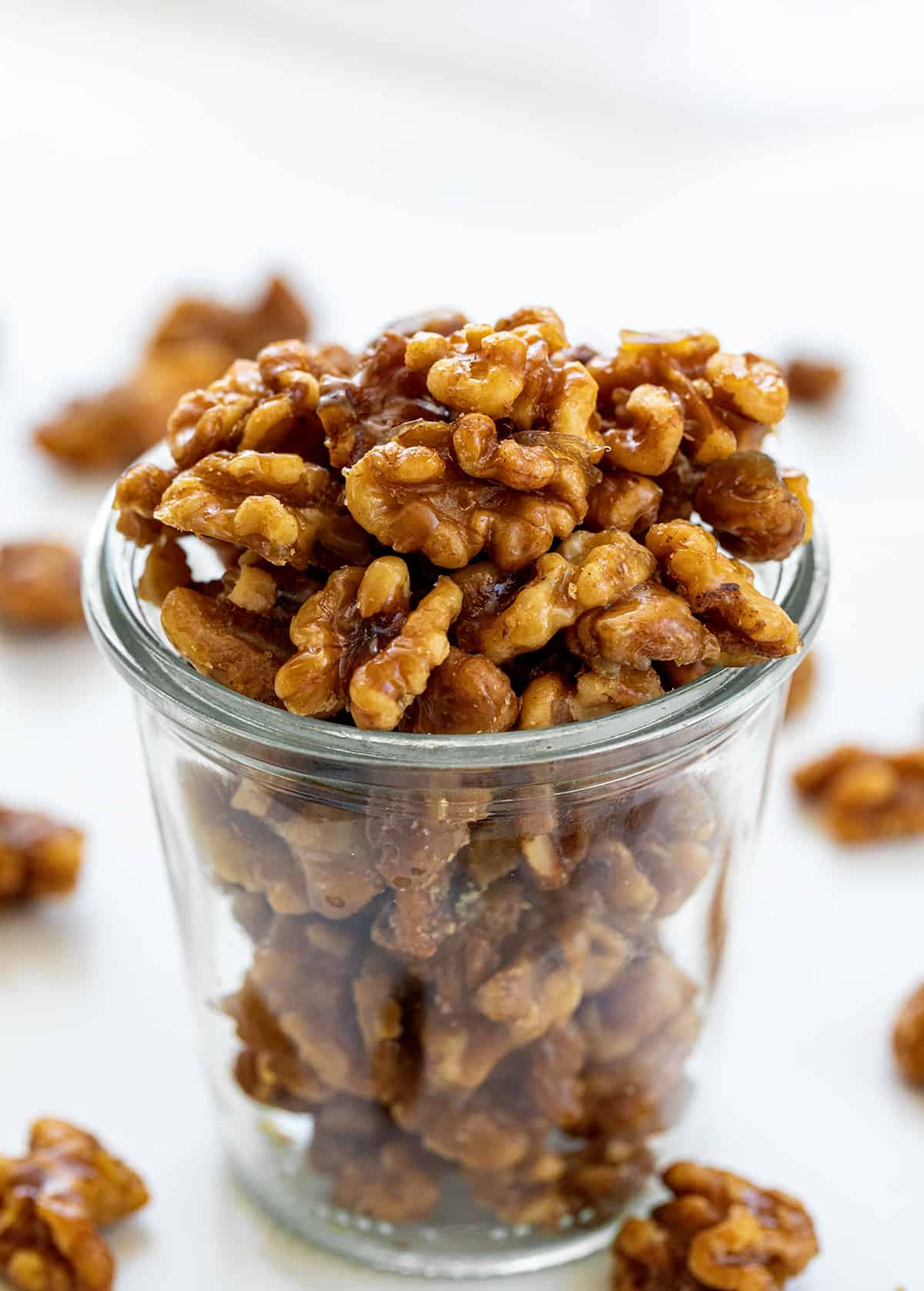 This is the ONLY candied walnut recipe you will ever need!! Candied Walnuts are walnuts that have been coated with a buttery sweet mixture and then baked to a crunchy golden brown. They are an addicting snack on their own, but also a delicious topping for salads and desserts. And, they can even be made in an air fryer! Jar of Candied Walnuts with Some Scattered Around it.