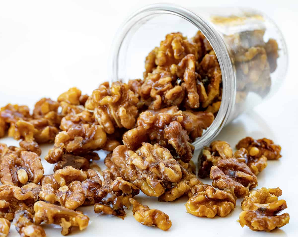 This is the ONLY candied walnut recipe you will ever need!! Candied Walnuts are walnuts that have been coated with a buttery sweet mixture and then baked to a crunchy golden brown. They are an addicting snack on their own, but also a delicious topping for salads and desserts. And, they can even be made in an air fryer! Jar of Candied Walnuts Tipped Over and Some Falling out Onto the Counter.