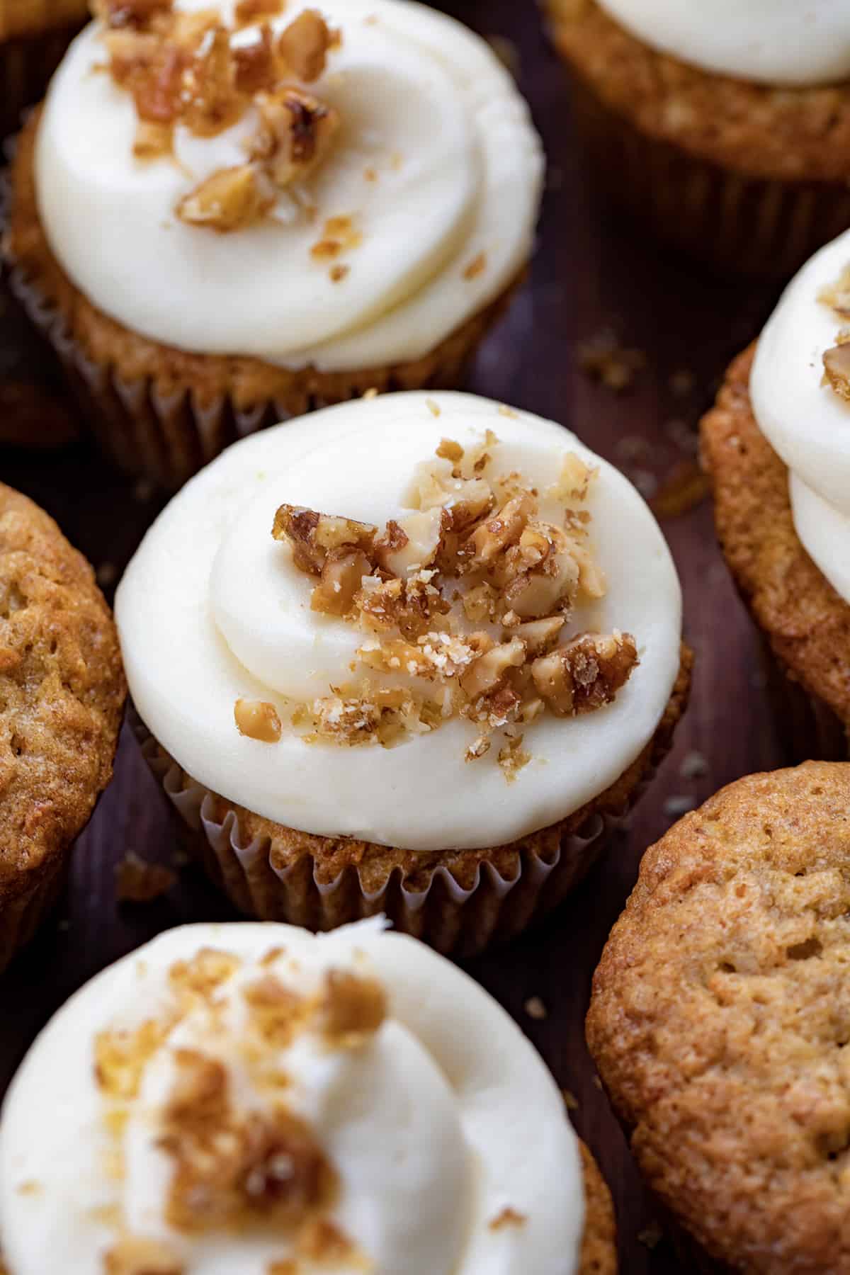 Carrot Cake Cupcakes are tender cupcakes loaded with carrots, walnuts, and pineapple that are topped with the best cream cheese frosting! The cupcakes give you all of the flavors of a cream cheese-frosted carrot cake but in a cupcake! The top is slightly crispy and the inside is a soft, tender crumb that is loaded with flavor. Be sure to have them on hand whenever you are craving carrot cake! Close up of Carrot Cake Cupcake with Cream Cheese Frosting with Candied Walnuts.