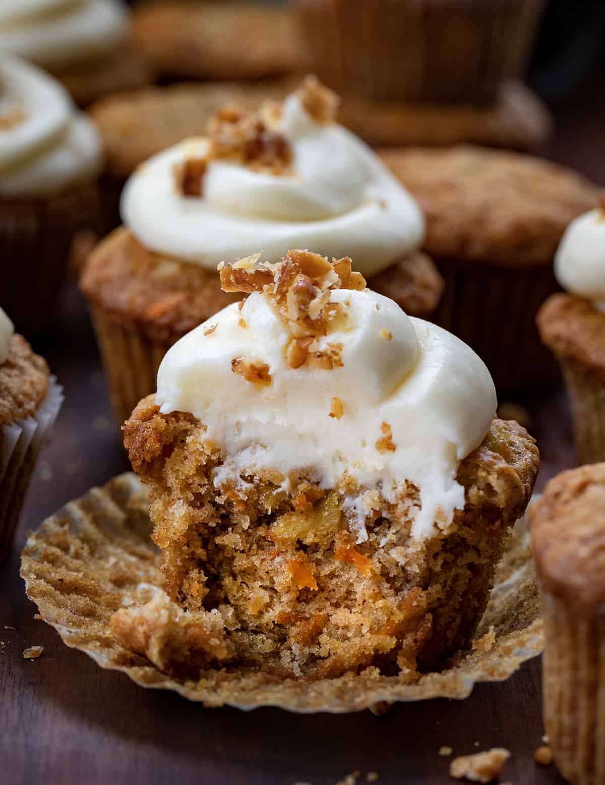 Carrot Cake Cupcakes are tender cupcakes loaded with carrots, walnuts, and pineapple that are topped with the best cream cheese frosting! The cupcakes give you all of the flavors of a cream cheese-frosted carrot cake but in a cupcake! The top is slightly crispy and the inside is a soft, tender crumb that is loaded with flavor. Be sure to have them on hand whenever you are craving carrot cake! Carrot Cake Cupcake Next to Each Other and One with Some removed Showing the Inside Texture.