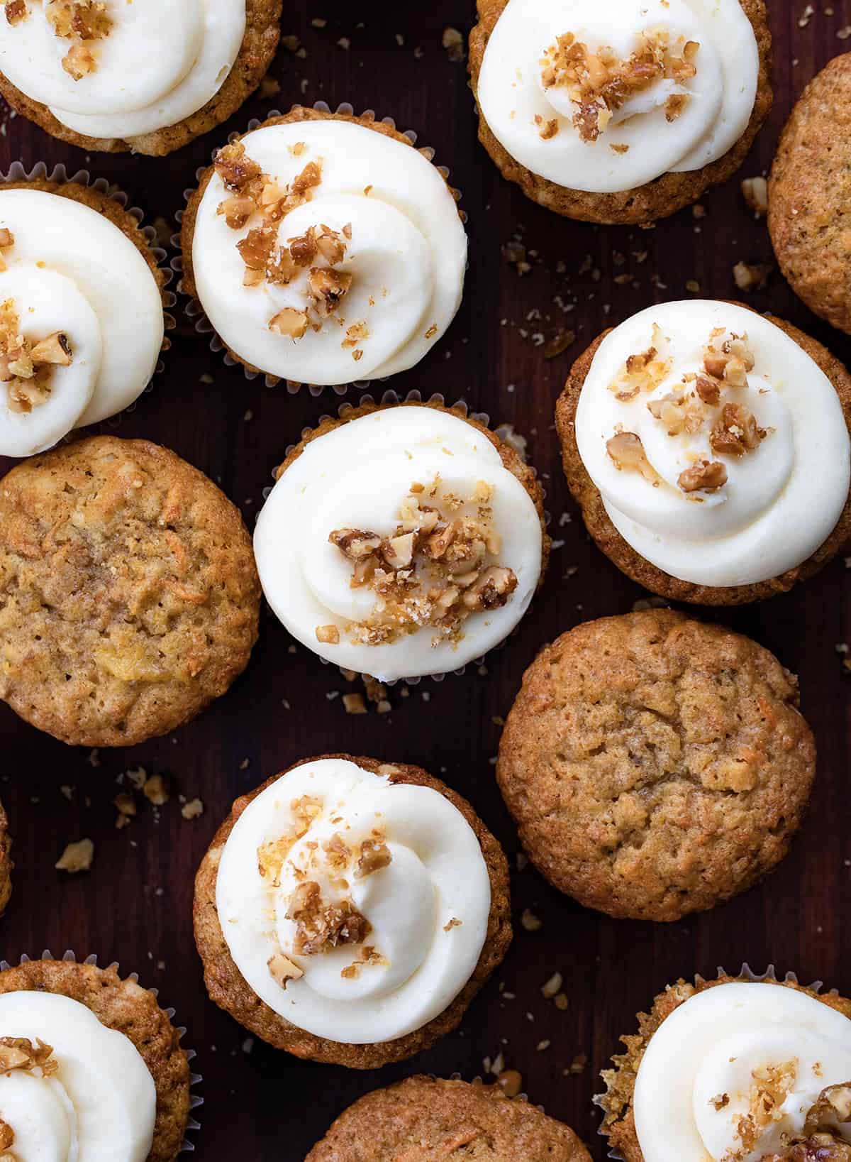Carrot Cake Cupcakes are tender cupcakes loaded with carrots, walnuts, and pineapple that are topped with the best cream cheese frosting! The cupcakes give you all of the flavors of a cream cheese-frosted carrot cake but in a cupcake! The top is slightly crispy and the inside is a soft, tender crumb that is loaded with flavor. Be sure to have them on hand whenever you are craving carrot cake! Looking down over Carrot Cake Cupcake Some with Cream Cheese Frosting and Candied Walnuts and Some Without.