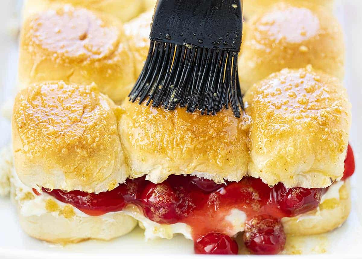 Cherry Cheesecake Sliders are a sweet, simple dessert that has all the flavors of cherry cheesecake tucked in between Hawaiian rolls and drizzled with a cream cheese frosting! Dessert Sliders, Dessert, Easy Desserts, Holiday Desserts, Memorial Day Dessert, July 4th Dessert, Sliders, Cherry Cheesecake Sliders, Cherry Cheesecake Desserts, i am baker, iambaker, baking, recipes Spreading Topping Over Cherry Cheesecake Sliders