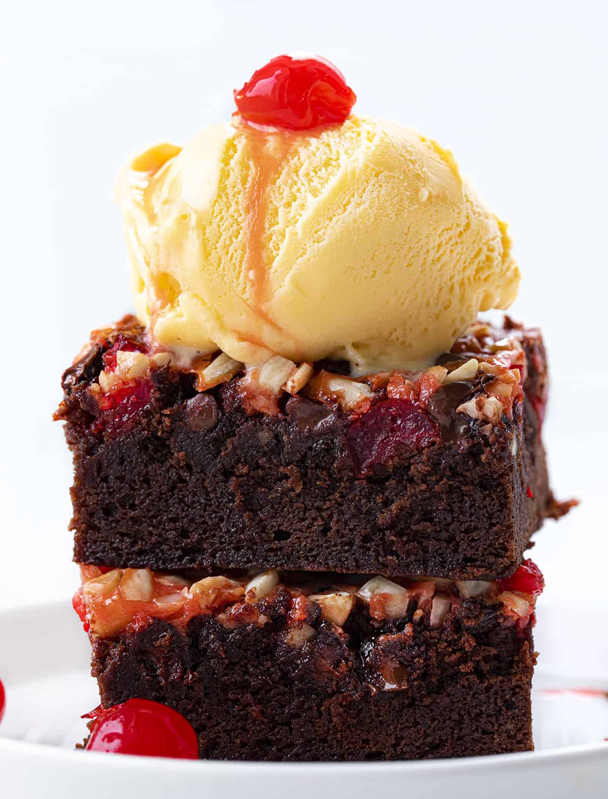 Cherry Chocolate Magic Brownies start with a brownie base topped and baked with maraschino cherries, chocolate chips, almonds, and sweetened condensed milk. It's like enjoying chocolate-covered cherries in a brownie! Stack of Cherry Chocolate Magic Brownies on a Plate with Ice Cream and a Cherry on Top.
