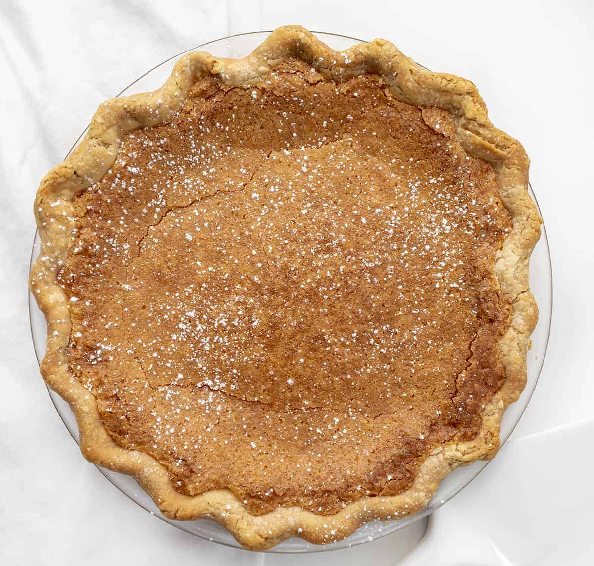 Chess Pie is a rich, sweet, and sugary classic pie that is made with ingredients you probably have on hand and baked in a flaky crust! Pie, Baking, Dessert, Chess Pie, Vintage Dessert, Classic Recipes, Classic Pie Recipes, Homemade Pie Crust, Rustic Pies, i am baker, iambaker Baked Chess Pie from Overhead on White Surface