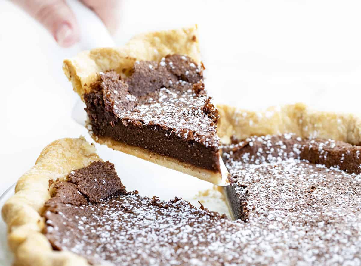 Chocolate Chess Pie is a fudgy chocolate pie filling made in a flaky crust that will satisfy all the chocolate lovers out there! The filling is thick, almost to the point of it being a brownie consistency. Lip smakin' delicious! Baking, Dessert, Chocolate Pie, Cheese Pie, Chocolate Chess Pie, Homemade Pie Crust, Store Bought Pie Crust, Easy Pie, Brownie Pie, Holiday Pie, Dessert Pie, Recipes, i am baker, iambaker Removing a Piece of Chocolate Cheese Pie from Pie Plate