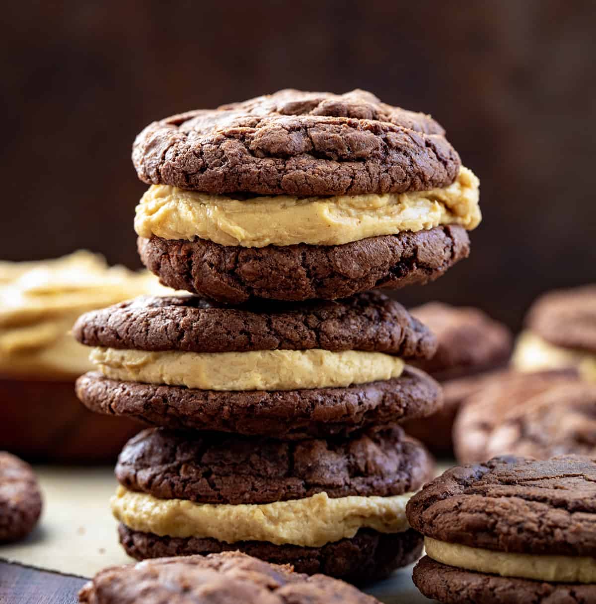 Chocolate Peanut Butter Sandwich Cookies are rich, chocolatey cookies filled with a homemade peanut butter frosting filling. The chocolate cookies are decadent enough to stand on their own with their crispy outside and soft, chewy center. (Trust me, I had a few!) But the added peanut butter filling was the perfect complement to the chocolate, making this one of my favorite sandwich cookies of all time. Stacked Chocolate Peanut Butter Sandwich Cookies on a Dark Cutting Board Surrounded by More Cookie Sandwiches.