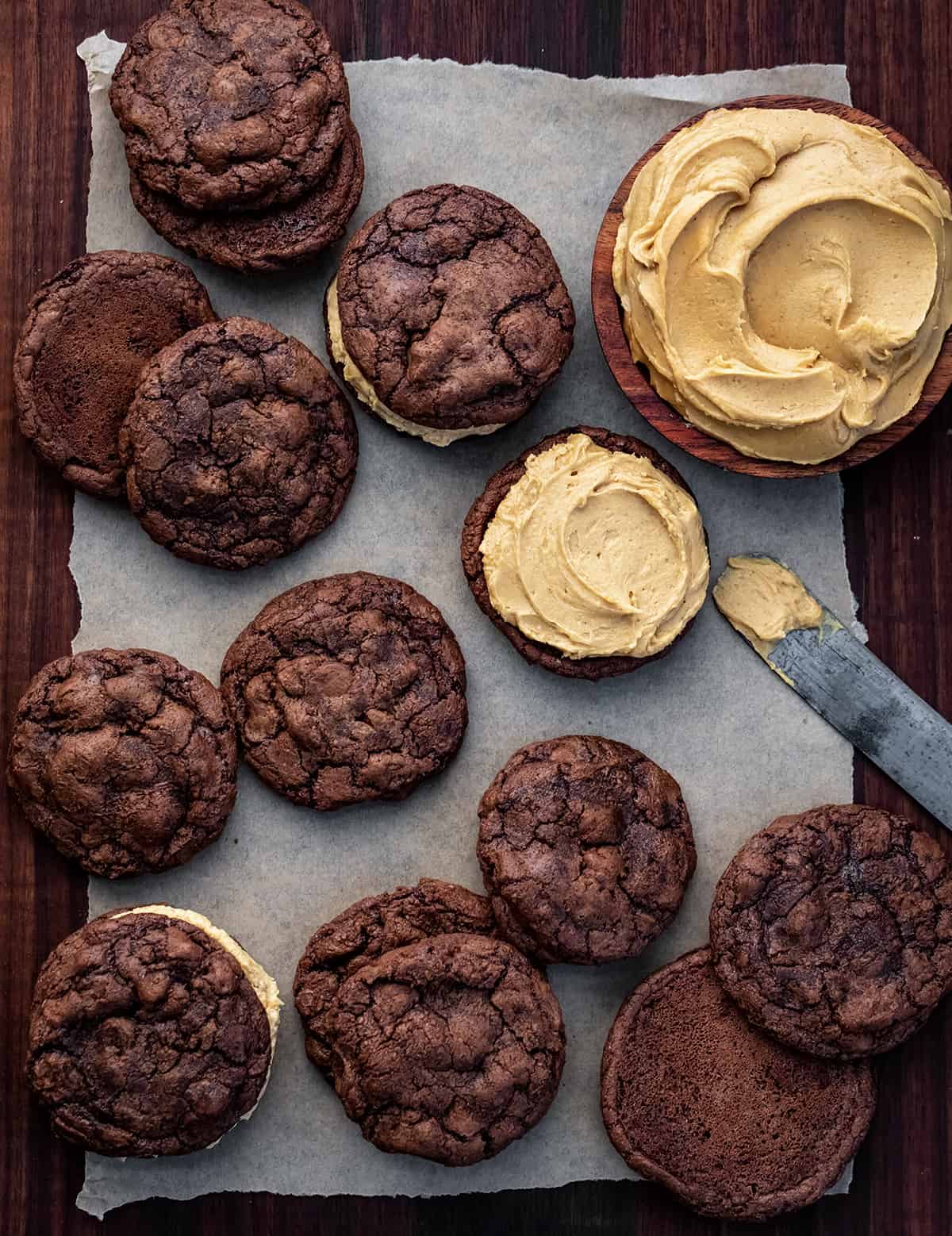 Chocolate Peanut Butter Sandwich Cookies are rich, chocolatey cookies filled with a homemade peanut butter frosting filling. The chocolate cookies are decadent enough to stand on their own with their crispy outside and soft, chewy center. (Trust me, I had a few!) But the added peanut butter filling was the perfect complement to the chocolate, making this one of my favorite sandwich cookies of all time. Cookies on a Dark Cutting Board with Peanut Butter Frosting and Adding Peanut Butter Frosting to Some Cookies.