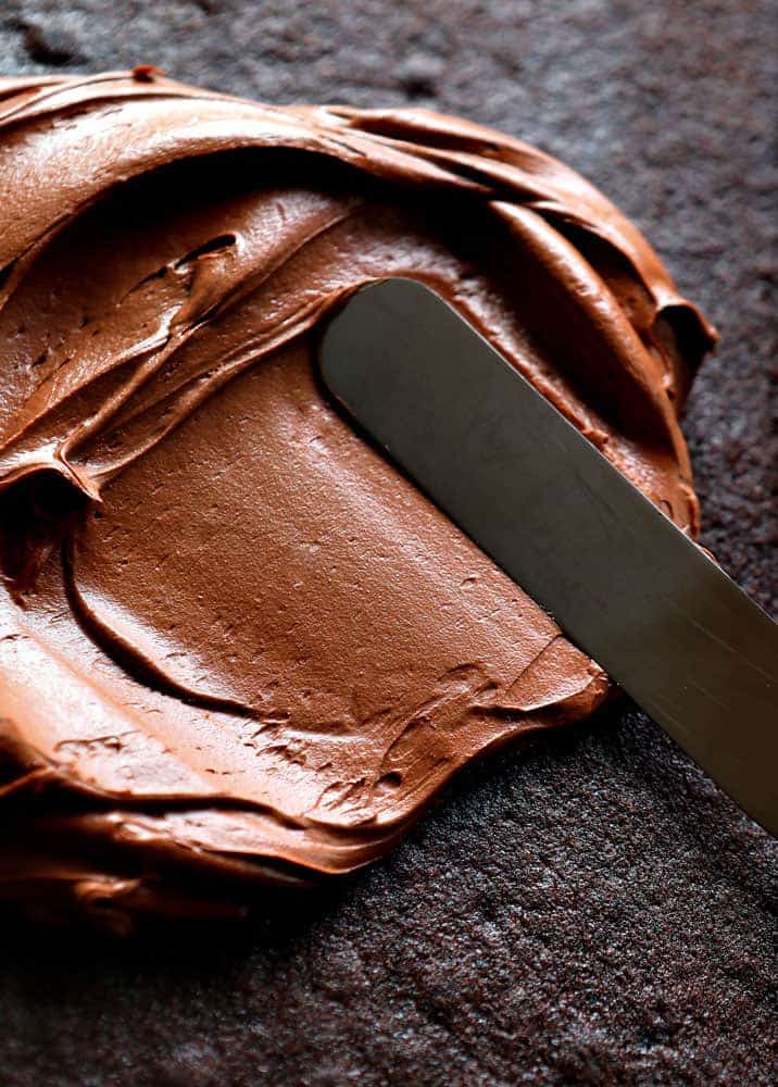 If you are looking for a UNIQUE recipe that packs a chocolate punch, this is the recipe for you! #chocolatecake #oldfashionedchocolatecake #recipes #baking #chocolate #perfectchocolatecake #chocolatefrosting #creamychocolatefrosting #iambaker Smoothing Frosting on Chocolate Cake