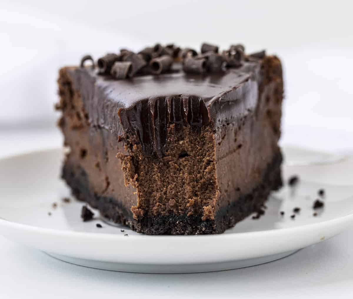 Chocolate Cheesecake is a chocolate lover's delight with an Oreo cookie crust filled in and baked with a rich and creamy chocolate cheesecake and topped with a chocolate ganache! Chocolate Cheesecake, Double Chocolate Cheesecake, Triple Chocolate Cheesecake, Ultimate Chocolate Cheesecake, Creamy Chocolate Cheesecake, How to Make Oreo Crust, How to Make Chocolate Cheesecake, baking, cheesecakes, i am baker, iambaker, Recipes One Slice of Chocolate Cheesecake with the tip removed showing the inside