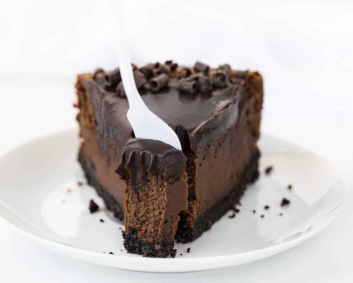 Chocolate Cheesecake is a chocolate lover's delight with an Oreo cookie crust filled in and baked with a rich and creamy chocolate cheesecake and topped with a chocolate ganache! Chocolate Cheesecake, Double Chocolate Cheesecake, Triple Chocolate Cheesecake, Ultimate Chocolate Cheesecake, Creamy Chocolate Cheesecake, How to Make Oreo Crust, How to Make Chocolate Cheesecake, baking, cheesecakes, i am baker, iambaker, Recipes White Fork Removing a Bite from One Slice of Chocolate Cheesecake