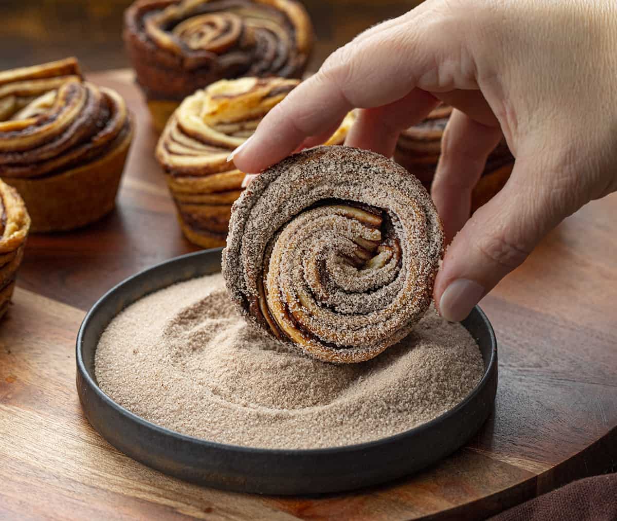 A cruffin is a cross between a croissant and a muffin that is rolled up like a cinnamon roll. It's a buttery, flaky dessert that is easier to make than it looks. Peppermint seems to be a part of the holidays, and these chocolate peppermint cruffins are no exception. In addition to the chocolate peppermint butter, I rolled each cruffin in more cocoa powder and sugar. They look fancy, but they are easy to make! Rolling Chocolate Peppermint Cruffin into Cinnamon Sugar.