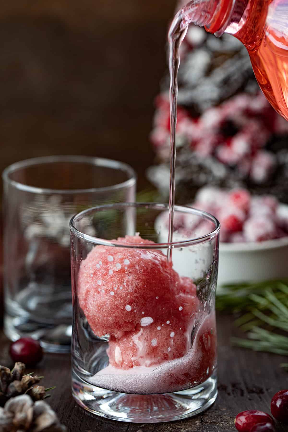Christmas Slush Mocktail is a refreshing and festive beverage that can be enjoyed by all ages. It's made with a mixture of cranberry juice, orange juice, and lemonade concentrate, which is then frozen and served topped with cherry lemon-lime soda. Pouring Cherry Soda into a Christmas Slush Mocktail.