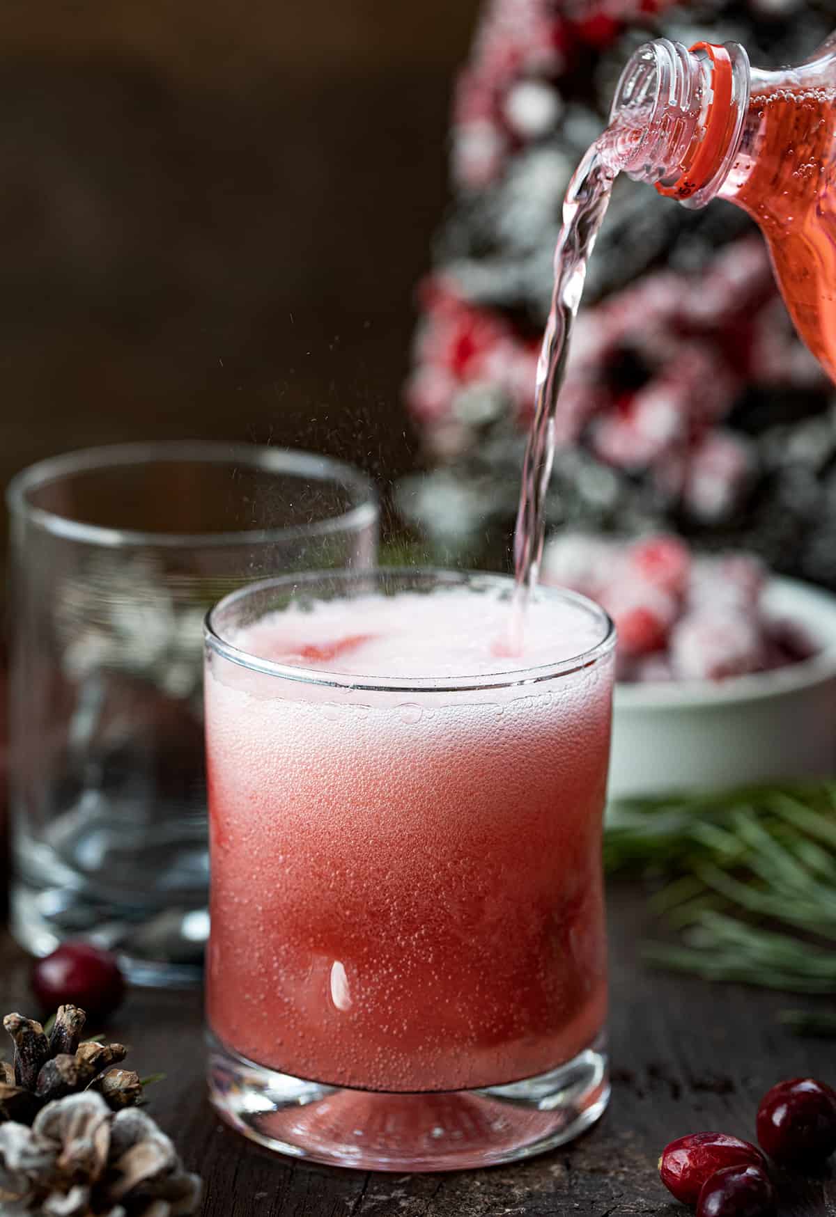 Christmas Slush Mocktail is a refreshing and festive beverage that can be enjoyed by all ages. It's made with a mixture of cranberry juice, orange juice, and lemonade concentrate, which is then frozen and served topped with cherry lemon-lime soda. Pouring Cherry Soda into a Christmas Slush Mocktail.