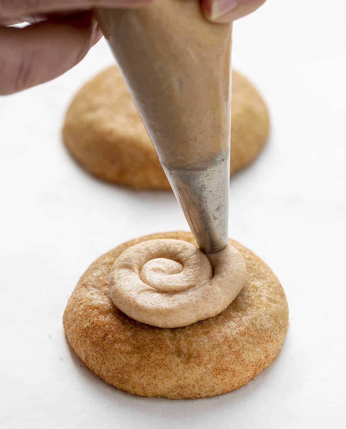 Churro Cookies are a Crumbl cookie copycat that are soft and chewy cinnamon sugar cookies topped with cinnamon buttercream. Copycat Cookies, Churro Cookies, Crumbl Cookie, Cinnamon Cookies, baking, Dessert, Fall Baking, Thanksgiving Cookie, Thanksgiving Dessert Recipes, New Years Dessert Cookies, Soft Cookies, i am baker, iambaker Piping Cinnamon Buttercream onto a Churro Cookie