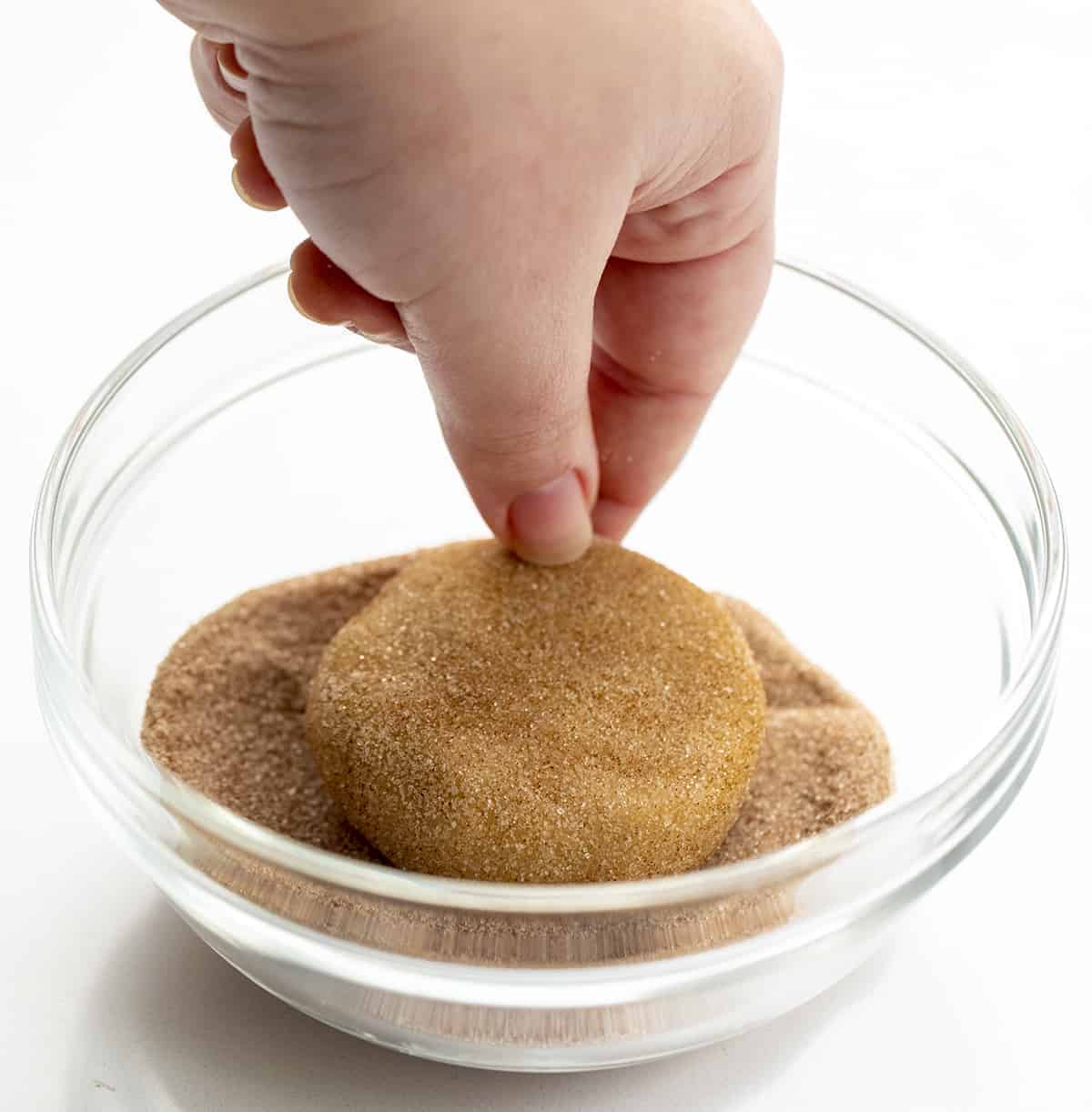 Churro Cookies are a Crumbl cookie copycat that are soft and chewy cinnamon sugar cookies topped with cinnamon buttercream. Copycat Cookies, Churro Cookies, Crumbl Cookie, Cinnamon Cookies, baking, Dessert, Fall Baking, Thanksgiving Cookie, Thanksgiving Dessert Recipes, New Years Dessert Cookies, Soft Cookies, i am baker, iambaker Hand Dipping Cookie Dough into Cinnamon Sugar for Churro Cookie