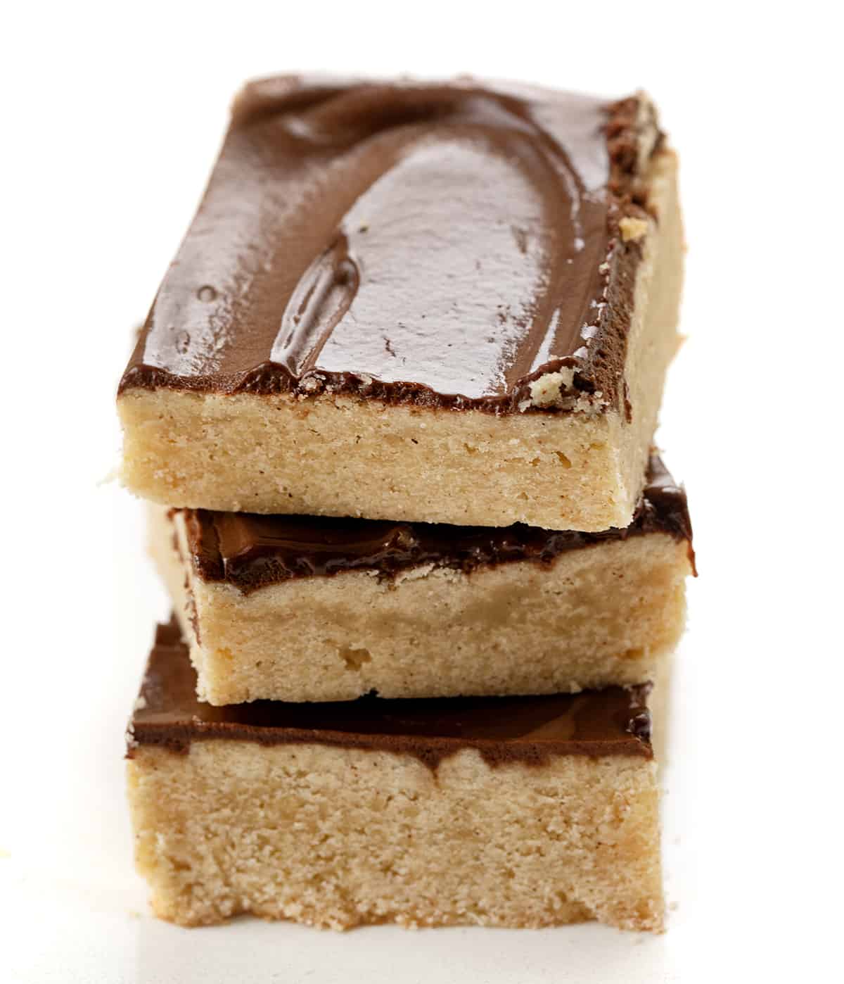 Cinnamon Shortbread Bars start with a buttery and crumbly shortbread cookie base flavored with cinnamon, topped with a whipped chocolate ganache. The ganache adds a rich and decadent layer that complements the cinnamon in the shortbread. Cinnamon Shortbread Bars Stacked on a White Counter.