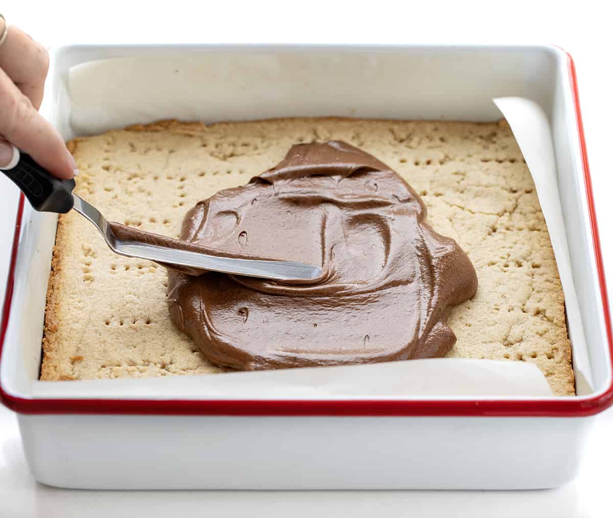 Cinnamon Shortbread Bars start with a buttery and crumbly shortbread cookie base flavored with cinnamon, topped with a whipped chocolate ganache. The ganache adds a rich and decadent layer that complements the cinnamon in the shortbread. Spreading Chocolate Over Cinnamon Shortbread Bars.