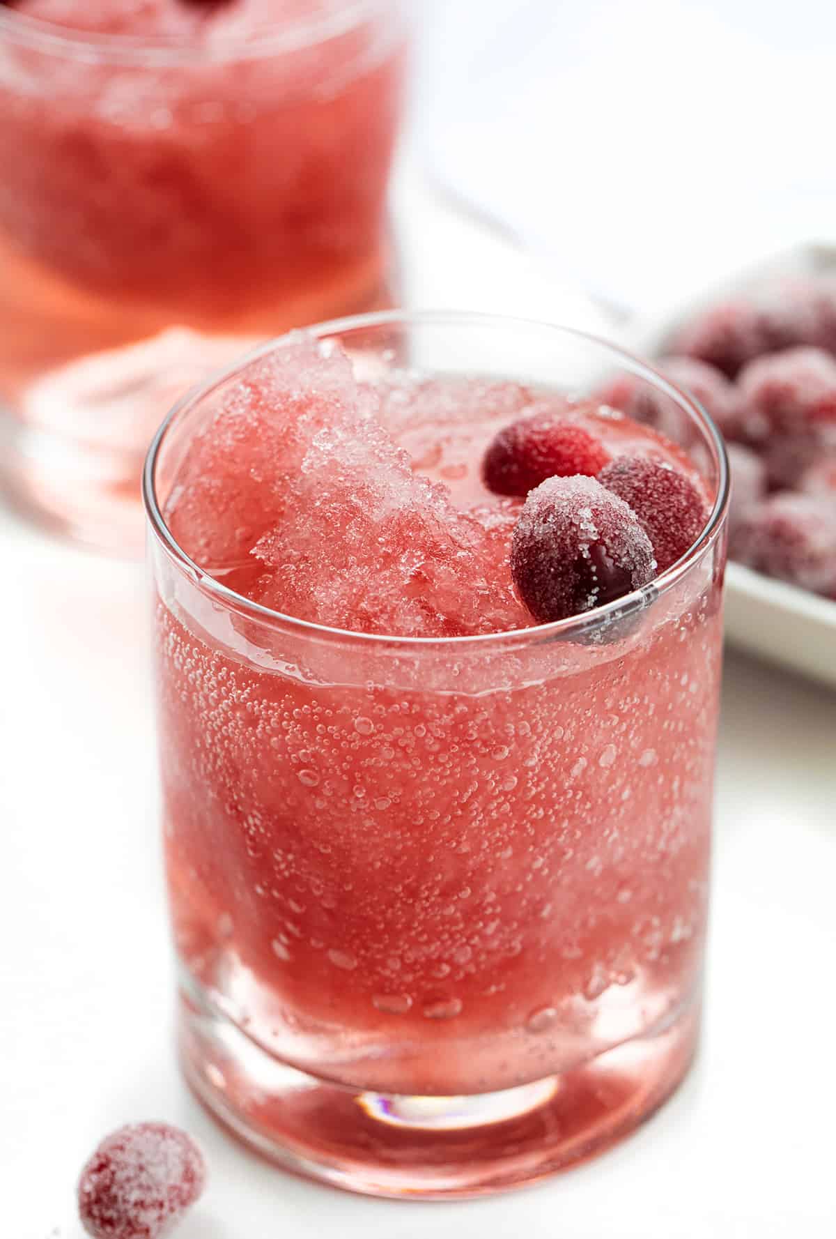 This Cranberry Slush is an adult beverage that is a holiday drink, but would also be delicious in the summertime, so don't forget about it. It's a festive and refreshing drink to serve with a lovely red color from the cranberries. Plus, the lemon-lime soda gives it some carbonation for a few bubbles. Serve it in a large punch bowl and let your guests help themselves! Cheers! Glasses of Cranberry slush with Sugared Cranberries.