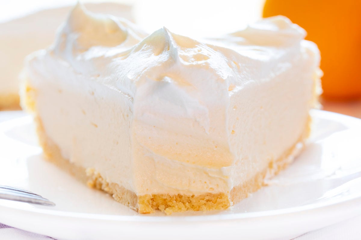 The best no-bake desserts to get your sweet tooth through the summer! no bake, no bake desserts, desserts, recipes, cheesecake, cookies, bars, cake, pudding, mousse, puppy chow, muddie buddies, rice krispy bars, dessert, memorial day dessert, labor day desserts, i am baker, iambaker Orange Creamsicle Pie on Plate with One Bite Removed Showing Inside.