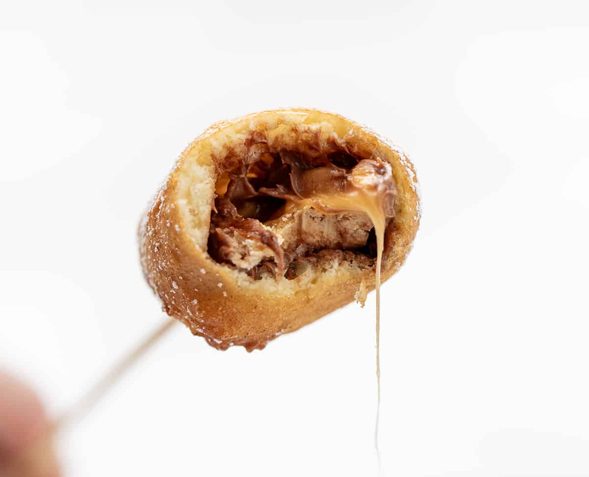 Deep Fried Snickers are fun and indulgent treats that combine the rich and gooey texture of a Snickers bar with a deep-fried golden exterior. Then, they are dusted with confectioners' sugar for beauty, but that is definitely an optional step! Serving them on a stick is a playful twist that adds to the overall experience, bringing a touch of that State Fair-like charm! Bit Into Deep Fried Snickers on a Skewer.