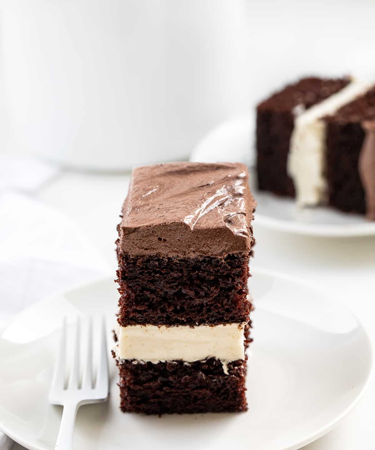 Ding Dong Sheet Cake is a decadent dessert with two layers of chocolate cake sandwiched together with a creamy filling and topped with chocolate frosting. The finished cake resembles a giant, elevated version of the popular chocolate-coated snack cake known as a "Ding Dong." It makes for a stunning and indulgent treat that is sure to delight chocolate lovers! Pieces of Ding Dong Sheet Cake on White Plates.