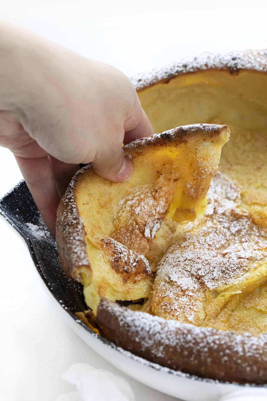 Dutch Baby Pancakes, also known as German or Puff pancakes, is like a combination of a crepe, a pancake, and a popover, all in one. It's a wonderful breakfast or brunch treat. Dutch Baby, German Pancake, Breakfast, recipes, i am baker, iambaker Hand Picking up Dutch Baby Pancake