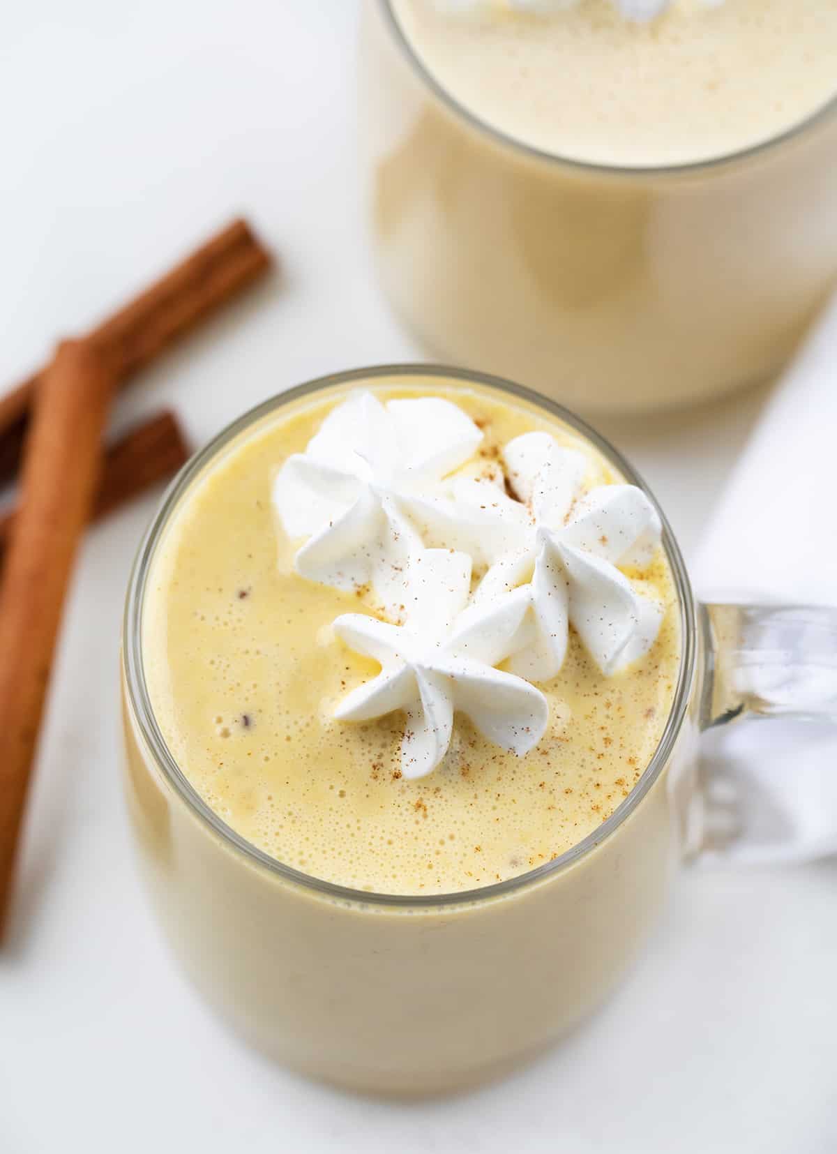 Eggnog is a creamy, egg-yolk-based holiday drink with just the right amount of spice that can be made with or without alcohol. It's delicious either way! And, when you make your own batch, you know exactly what is going into it without all the added preservatives. Better yet, you can adapt the recipe for all ages, making it a Christmas mocktail recipe if you leave out the alcohol. Glass mugs filled with eggnog and topped with whipped cream.